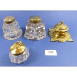 A group of four decorative brass and glass inkwells including one with stirrup to lid