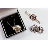A silver horseshoe brooch plus another unmarked brooch and a silver heart form locket necklace