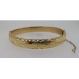 A 9ct gold hinged bangle with engraved decoration, 10g