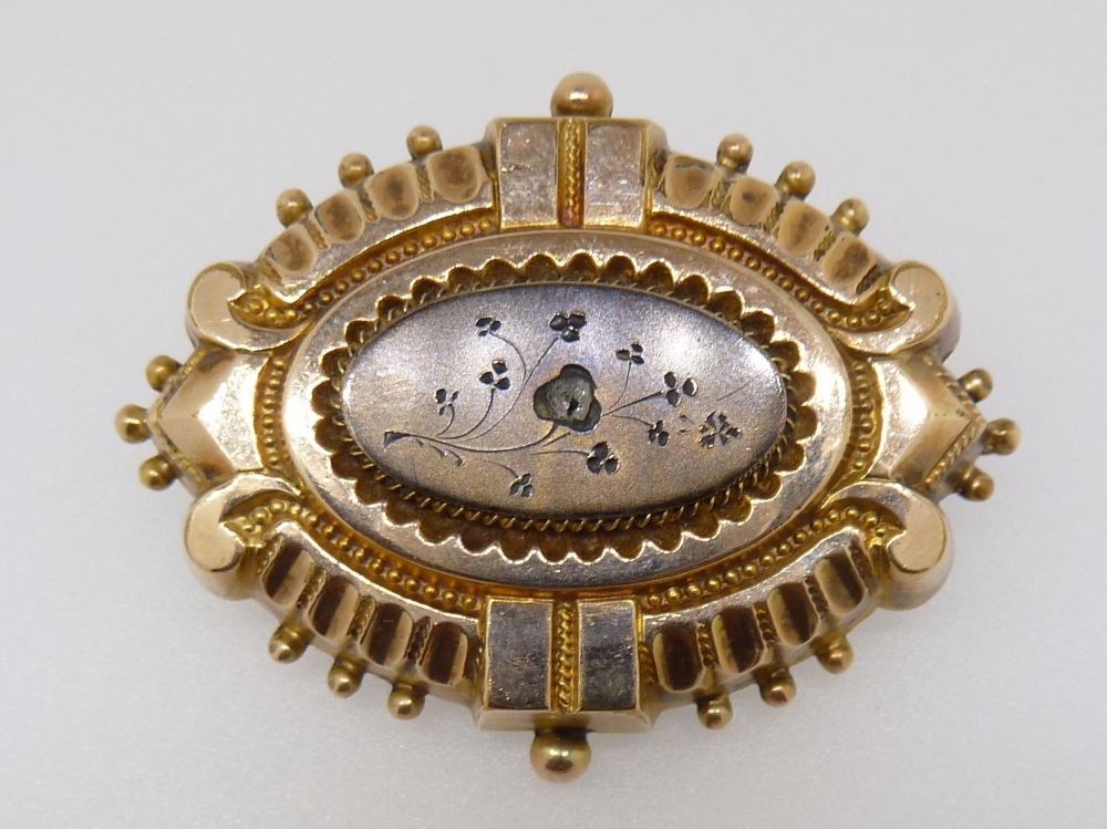 A Victorian yellow metal fronted oval brooch with embossed decoration and set chip diamond