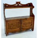 An Edwardian wall shelf and cupboard with all over inlaid decoration of Dutch children, flowers