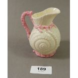 A Belleek shell form jug with pink coral handle, black mark to base 10cm