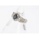 An 18ct white gold sapphire and diamond cluster ring, oval mixed cut sapphire surrounded by eight