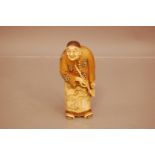 A Japanese late Meiji period carved ivory figure of an elder, 14cm, with red lacquer panel to