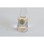An emerald and diamond cluster ring, claw set emerald, oval mixed cut surrounded by a bezel of