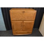 An Ercol fall front oak cabinet, having fitted interior with cupboard under and frieze plinth