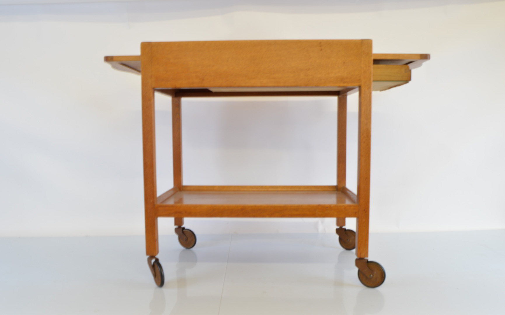 An early to mid 20th Century two tier oak trolley, on metal and rubber castors, with pull out