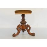 A walnut carved adjustable piano stool, with three bracket scroll feet on pedestal stem, rotating