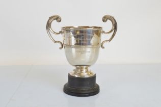 An Edwardian twin handled silver trophy cup, with high scroll handles, on ebonised plinth base,
