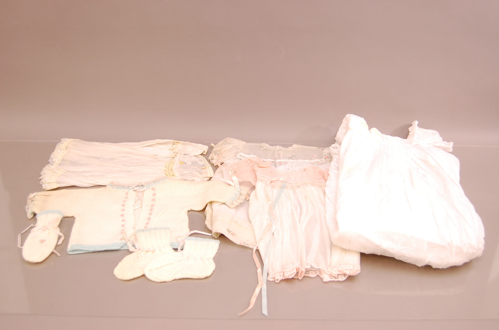 A collection of late 19th/early 20th century dolls clothing, including a knitted cardigan, gloves