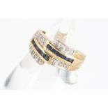 A continental yellow metal diamond and sapphire cross over ring, the channel set sapphires flanked