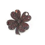 An antique garnet four leaf clover brooch, set with circular and rose cut gem stones, on a silver