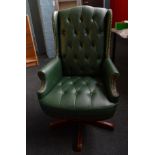 A green leather effect button back swivel desk chair, having studwork to wings and scroll arms on