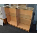 A contemporary open bookcase, having glass top and three glass adjustable shelves on plinth base,