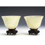 A pair of late 19th century Chinese Jadeite Jade plain bowls on hardwood stands, 9.8cm diameter,