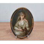 A 19th century hand painted Berlin ceramic plaque, depicting a girl with a lamp, in an oval gilt and