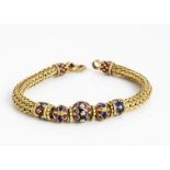 An Asian yellow metal and enamel bracelet, the central blue and red enamel beads, with woven