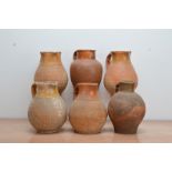 Six early 19th century partially salt-glazed terracotta jugs, of graduated sizes, the tallest 26cm