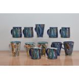 A large collection of Lea Phillips glazed stoneware mugs and jugs, with colourful glazed designs, of