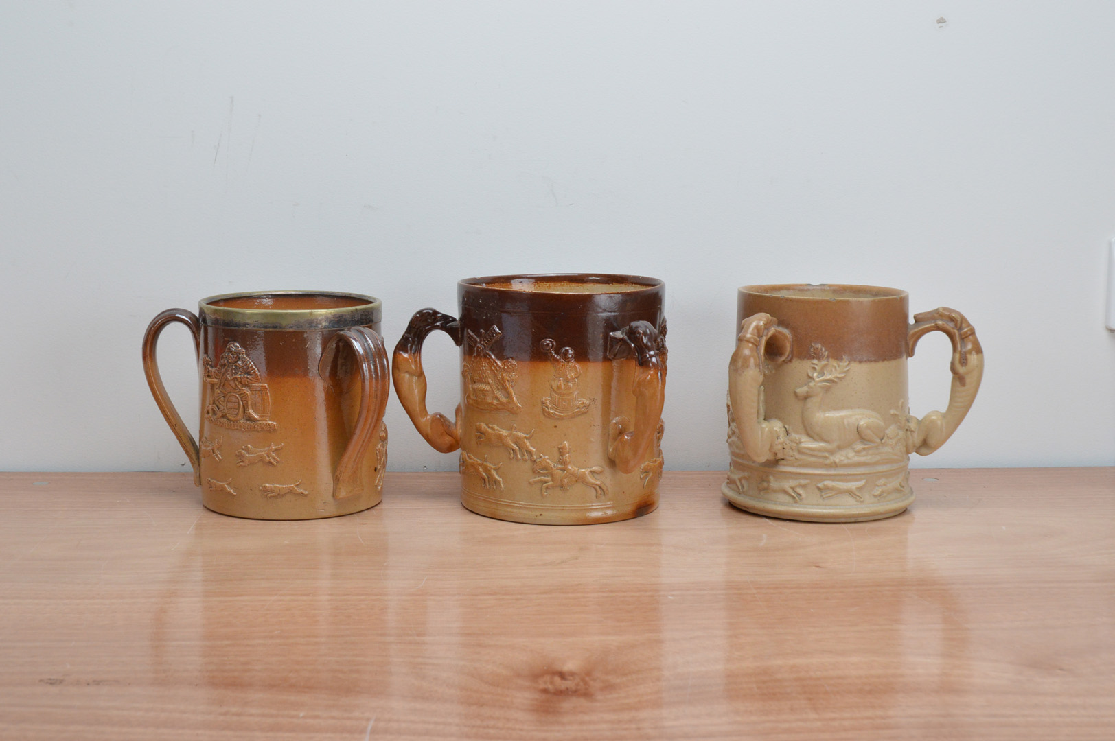 Three 19th century stoneware salt-glazed triple handled tankards, depicting hunting scenes, one with