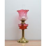 A cranberry glass and brass oil lamp, with some oil still present, 59cm high