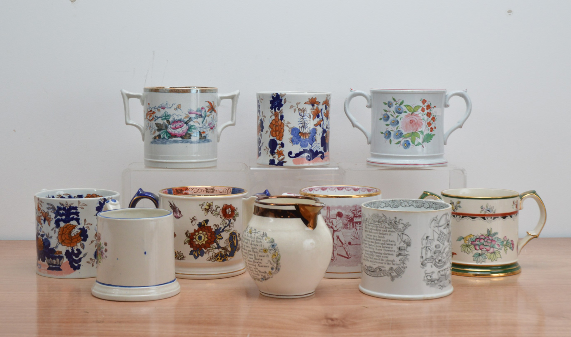 A collection of ceramic transfer tankards, including twin handled examples, three modern Wade