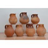 Seven early 19th century partially salt-glazed terracotta jugs, of slightly varying sizes, the