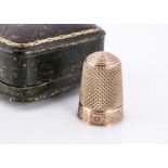 A yellow metal thimble, with engine turned and floral base, within a tooled leather case marked