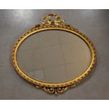 A gilt framed oval mirror, mounted with a bow, surmounted with scrolls, bevelled mirror plate,