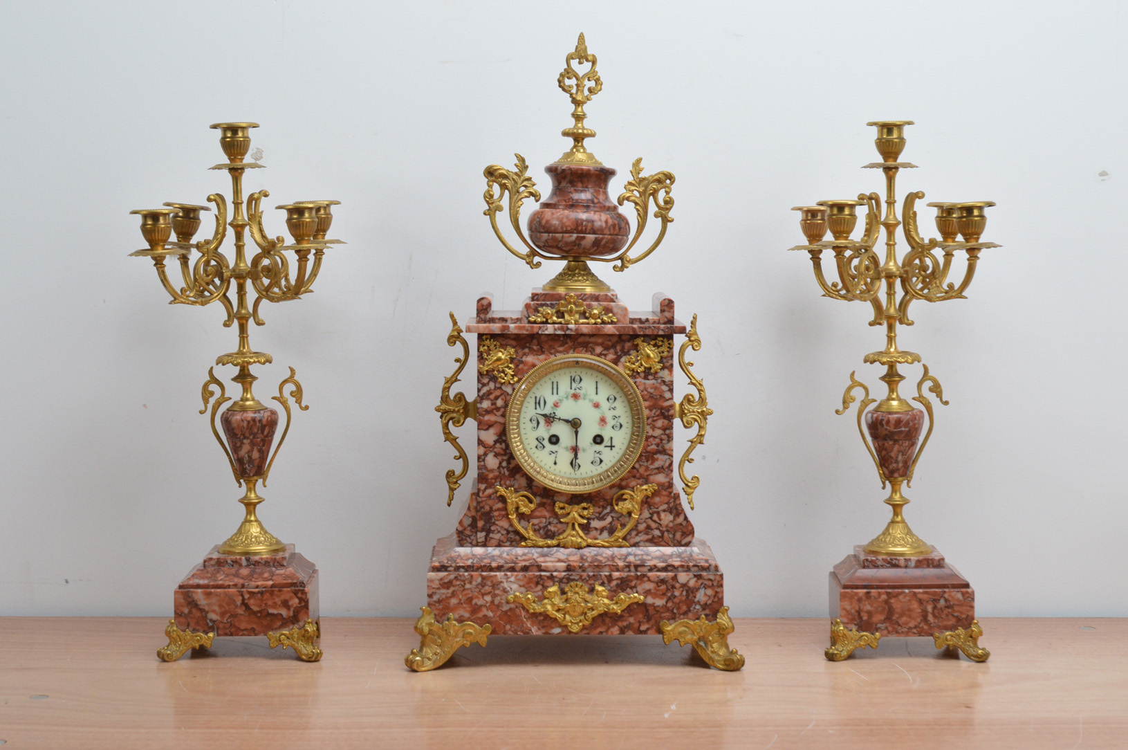 A late 19th century and later French red marble mantle clock garniture, the dial with Arabic