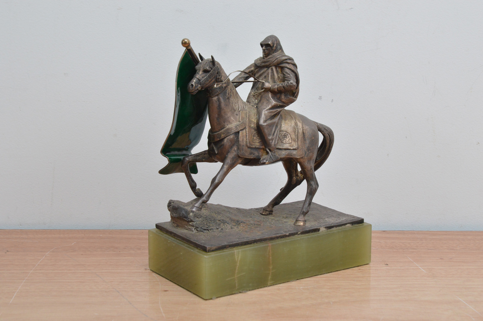 An art deco style early 20th century white metal medieval man on horseback, holding a green glass