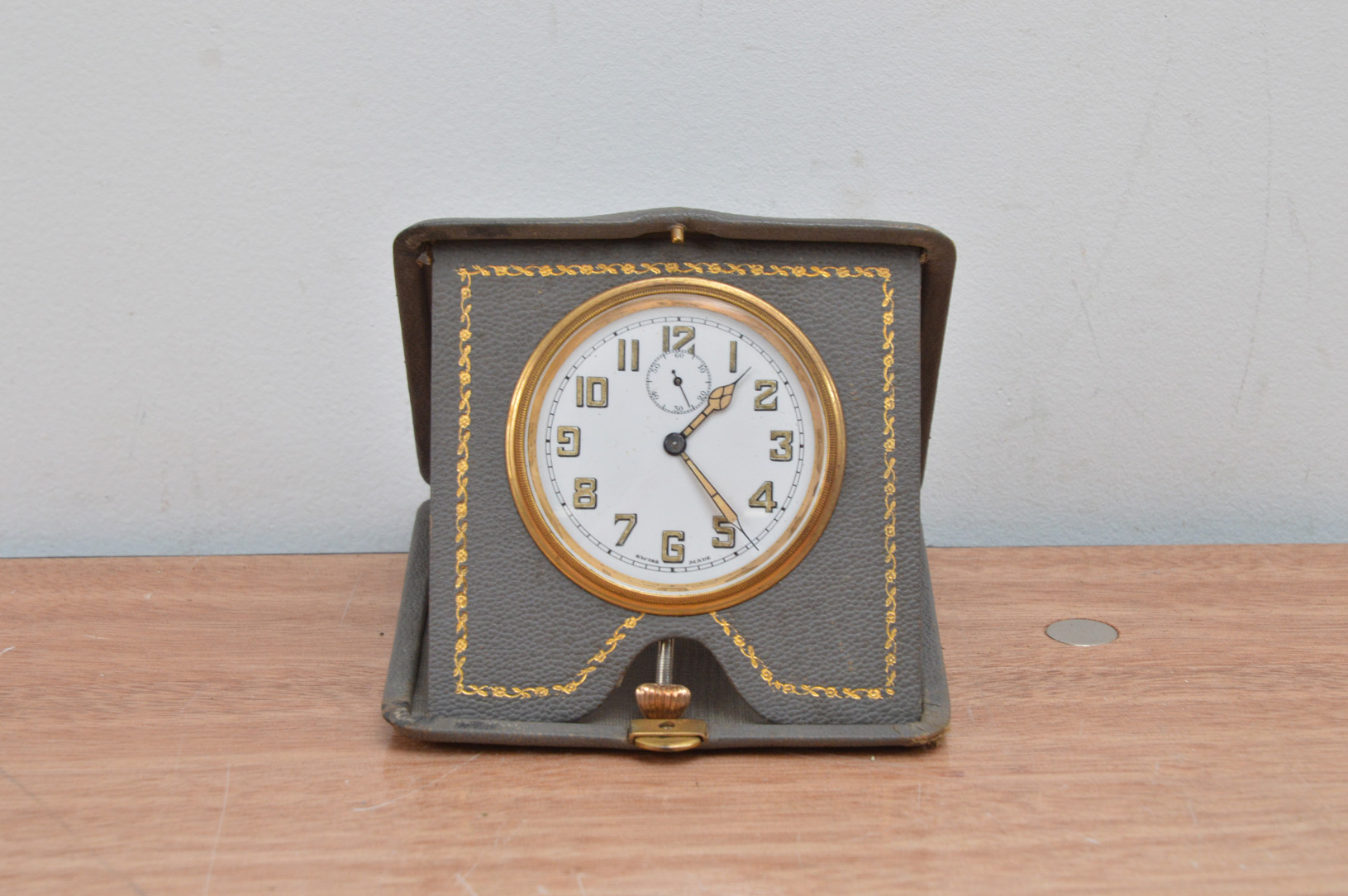 A 1930's travelling clock, in a foldable leatherette case, the dial with Arabic numerals, case