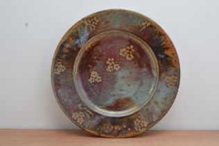 A large stoneware charger by John Calver, foliate and floral design, crimson, orange and blue,