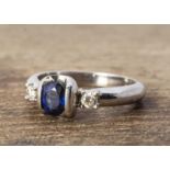 A continental white metal sapphire and diamond three stone ring, oval mixed cut sapphire in clasp