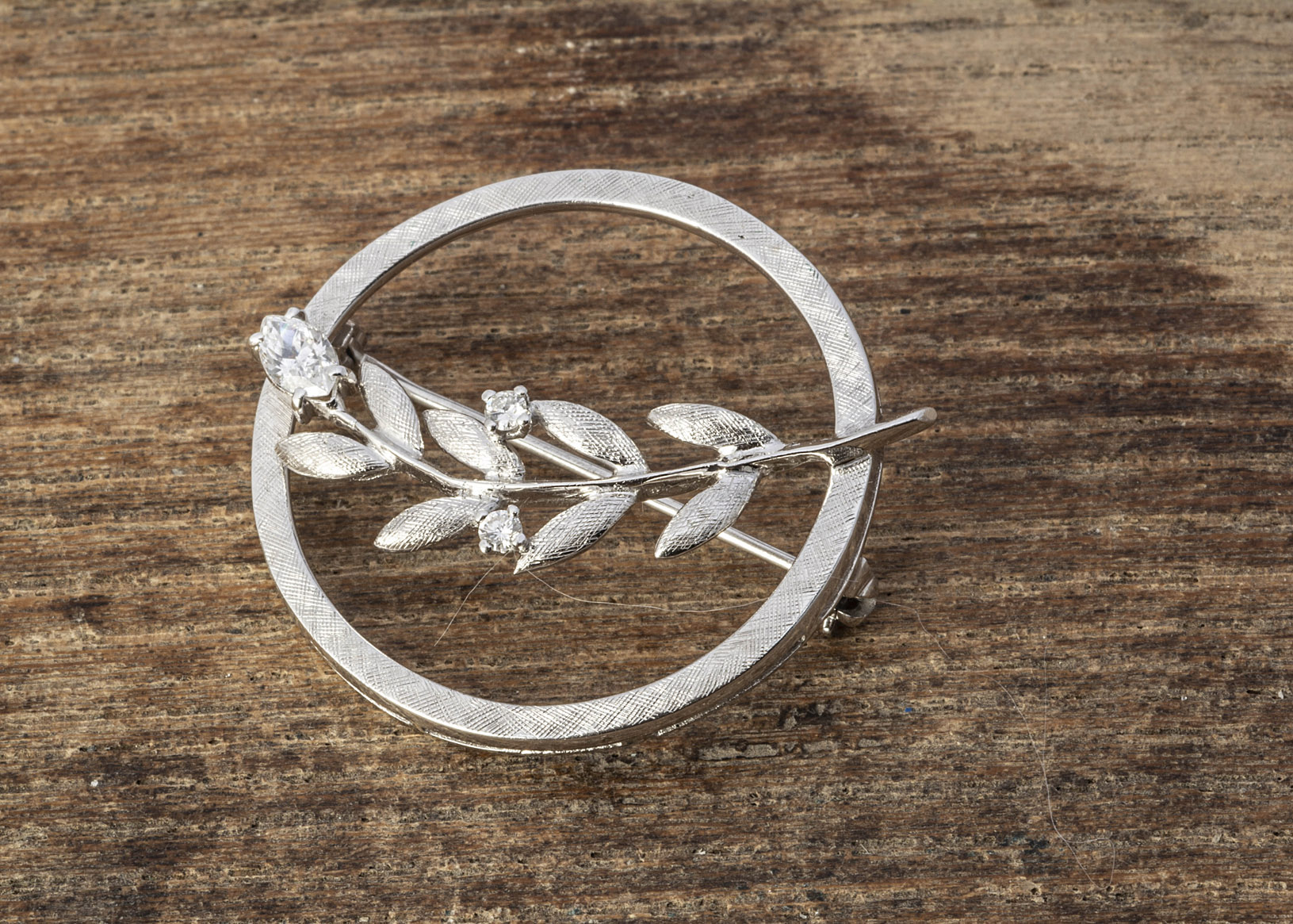 A continental white metal 14K marked circular brooch, of open worked leaf design, with white CZ