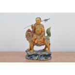 A Chinese carved wooden figurine, a gilt painted figure with a metal staff riding a mythical