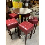 A circular metal framed bar table with wooden top and 6 red upholstered bar stools.