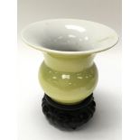 A small yellow vase with markings to base, on a wo