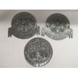 Three circular metal wall plaques comprising two M