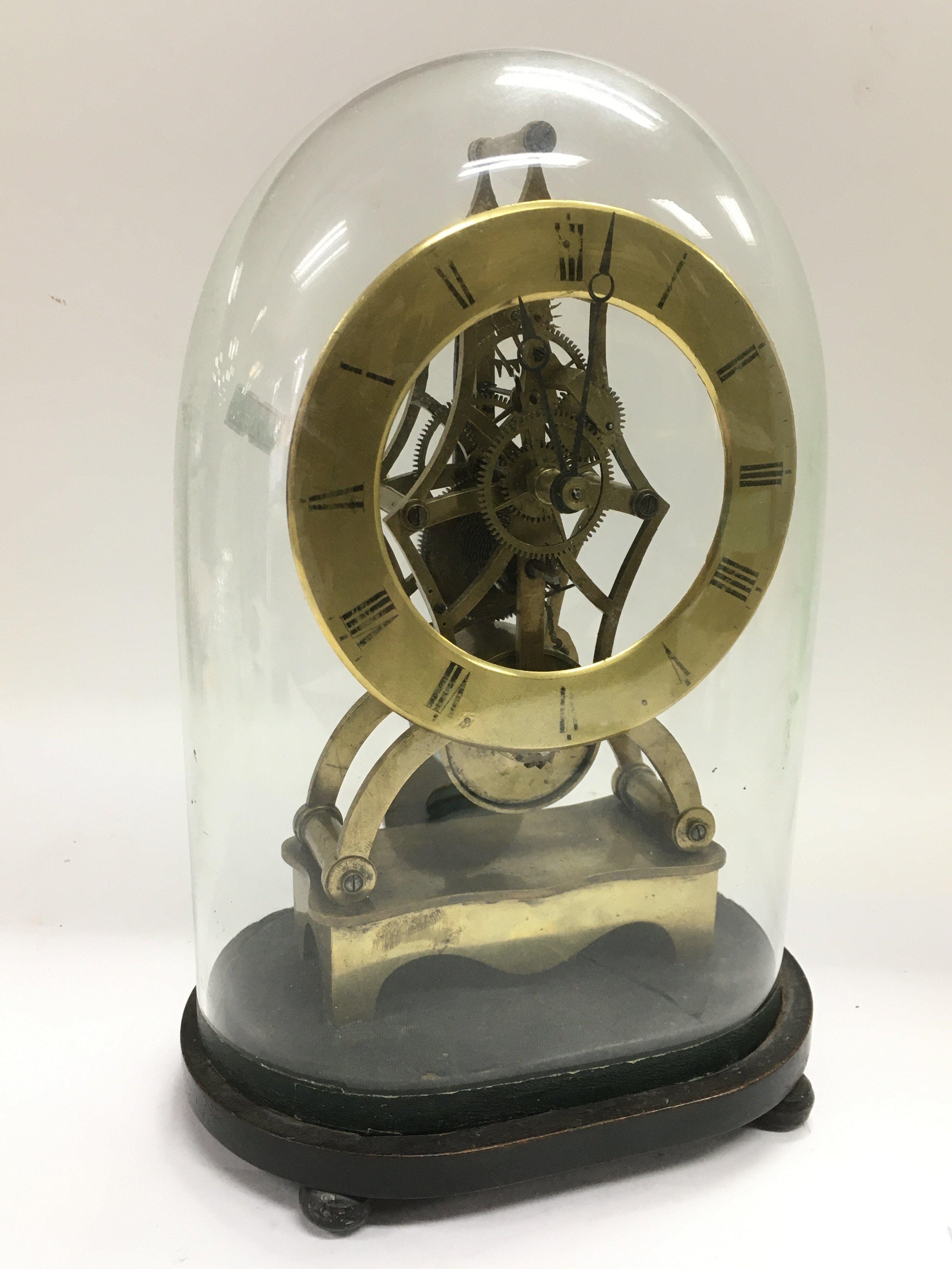 A brass skeleton clock under a glass dome, approx