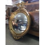 A gilt framed circular mirror the top surmounted w