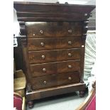 A large mahogany chest of drawers the top with an overhanging cornice above five drawers on turned