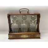 A carved Oak cased 3 bottle tantalus with engraved