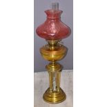 Victorian figural oil lamp with Corinthian column supports and cranberry glass shade, height 83cm