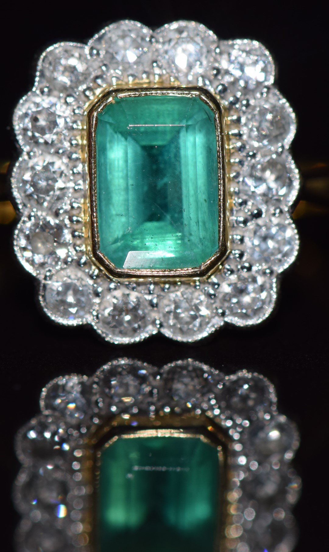 An 18ct gold ring set with an emerald cut emerald measuring approximately 1ct surrounded by 14