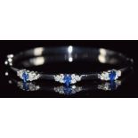 An 18ct white gold bangle set with three oval cut sapphires, each approximately 0.3ct and eighteen