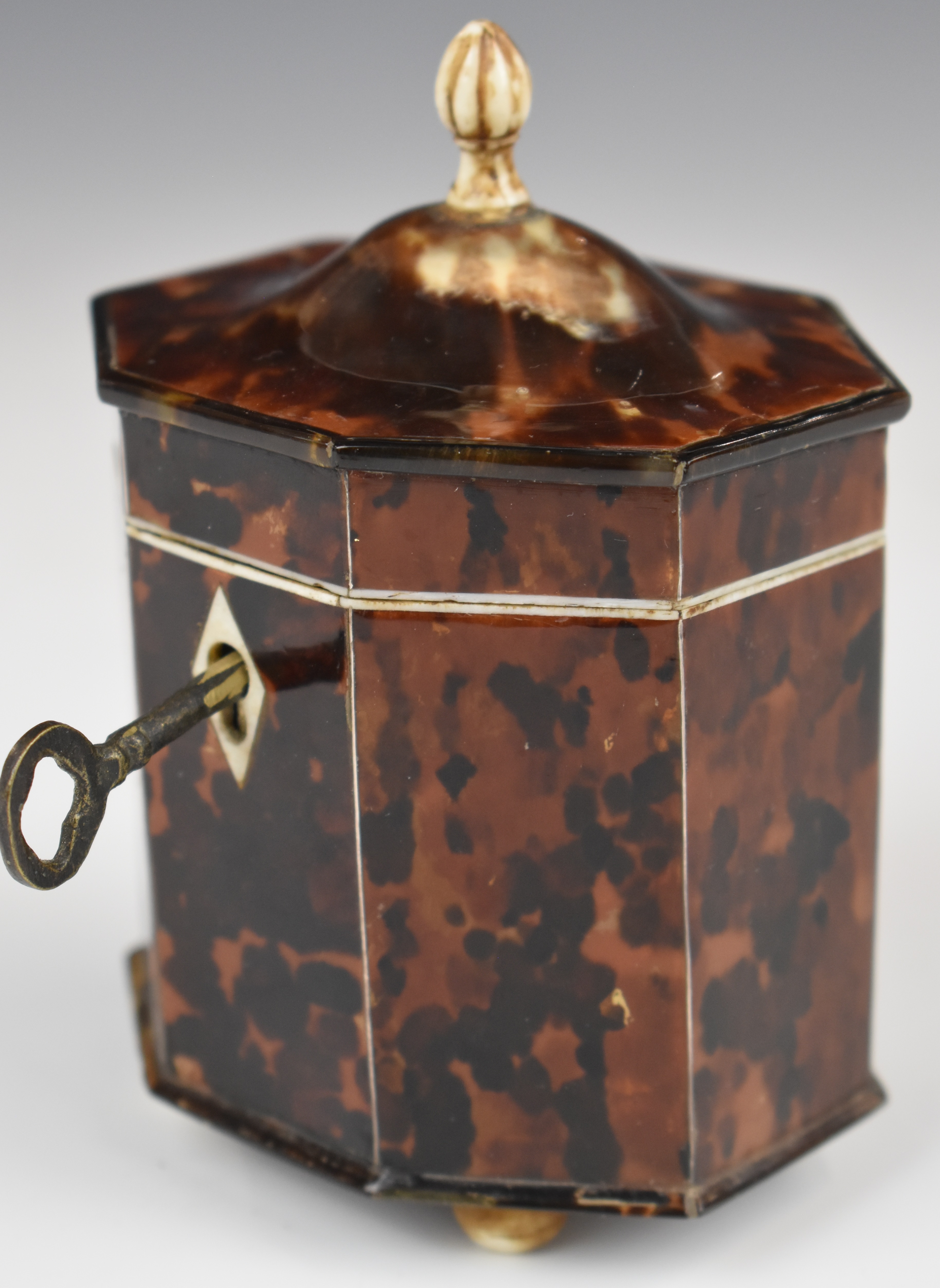 Octagonal tortoiseshell style tea caddy raised on four ball feet, height 12cm