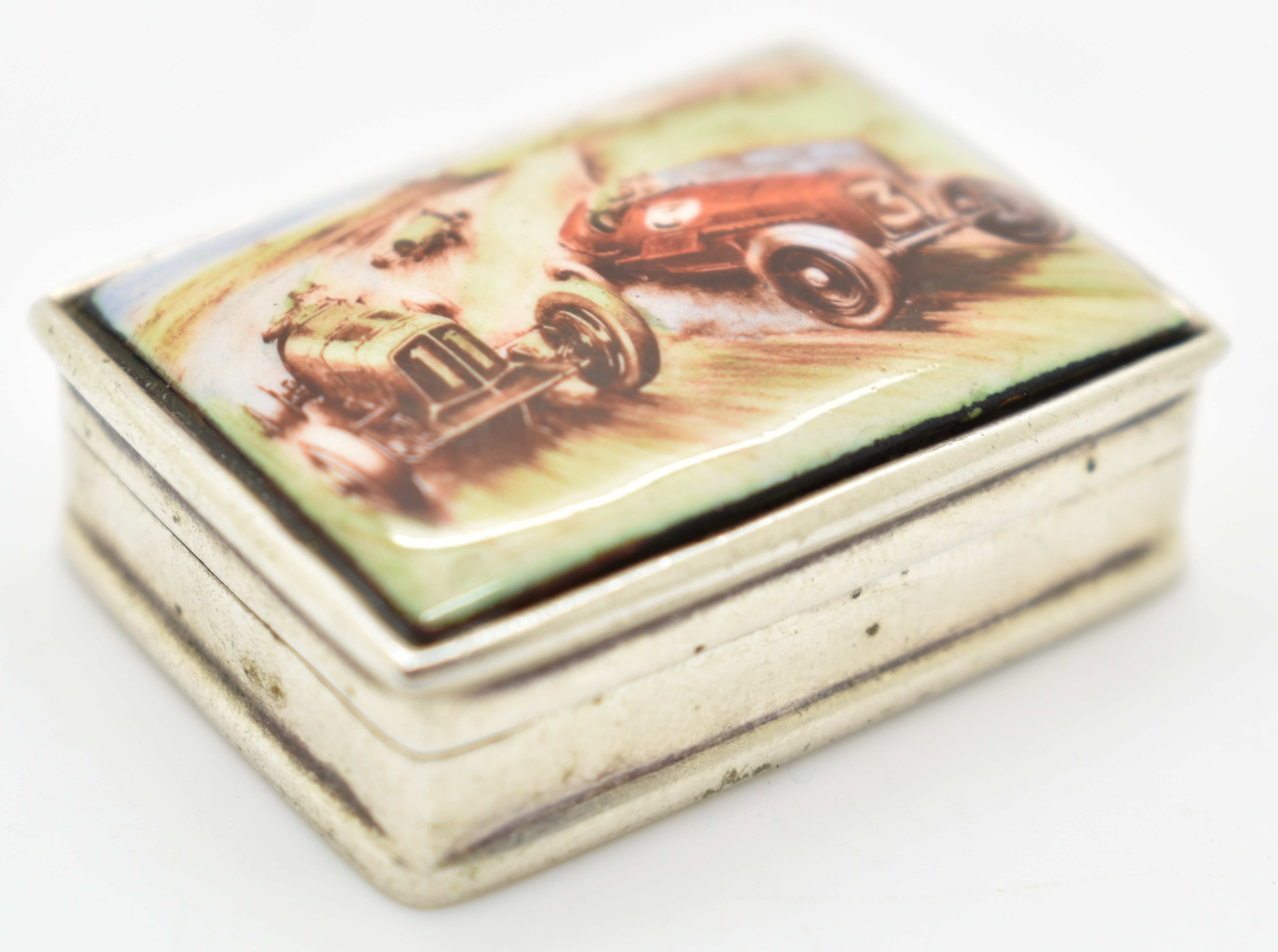 Hallmarked silver pill box with enamel decoration of a vintage motor car race to lid, London 2001,