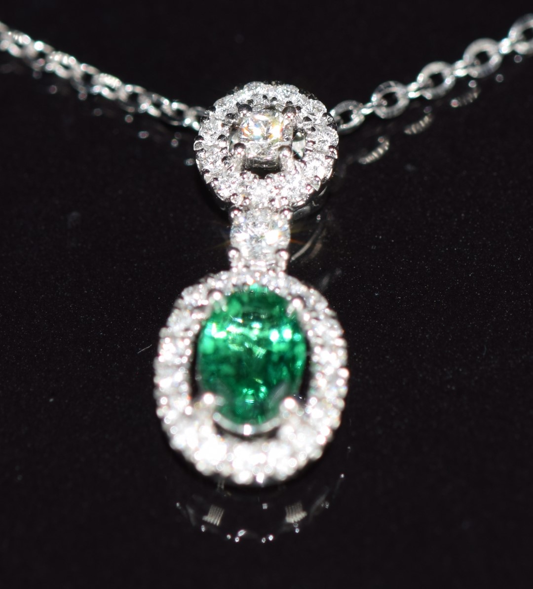 An 18ct white gold pendant set with an oval cut emerald of approximately 0.5ct surrounded by