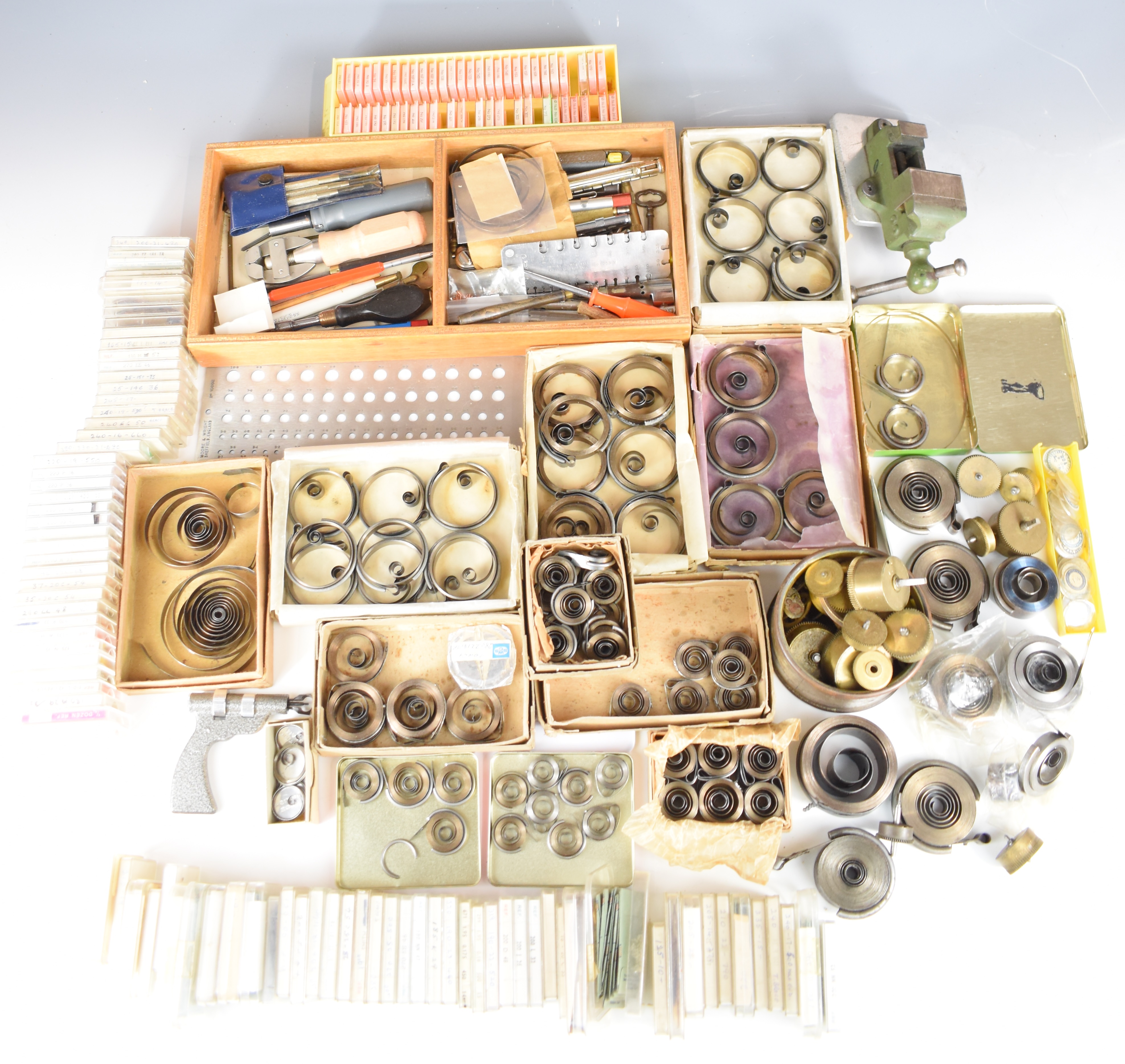 Collection of watch parts and tools including mainsprings, precision measuring devices, vices etc